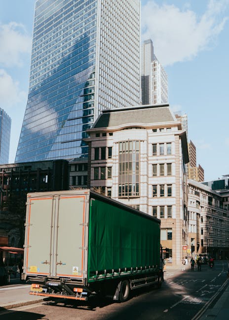 Several large cardboard boxes sealed with packing tape and labelled with 'Fragile' stickers and handling symbols are stacked on a doorstep outside a brick building, just in front of a closed, grey doo